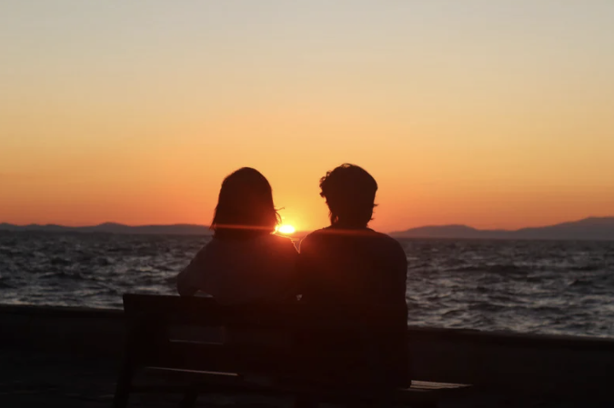 Silhouette of a Couple Sitting on Bench in Front of the Sea during Sunset