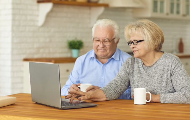 Happy senior couple sitting in front of laptop at home videocalling family and grandchildren. By studioroman